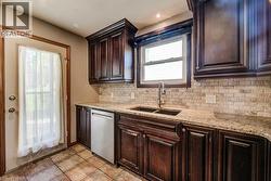 Dark wood cabinetry, granite countertops, dual basin sink with gooseneck faucet, stainless steel dishwasher, and tile flooring - 