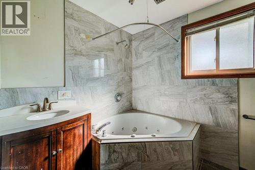 Jetted corner tub with tiled surround, wood-finish vanity with countertop, and an integrated sink - 3 Cora Drive, Kitchener, ON - Indoor Photo Showing Bathroom