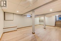 Versatile basement space featuring blonde wood-finish flooring, recessed ceiling lighting, and structural support columns - 