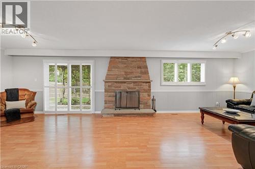 Wood-finish flooring, stone-clad fireplace with hearth, white window blinds, sliding glass patio door, and track lighting fixtures - 2535 Privet Crescent, Mississauga, ON - Indoor Photo Showing Living Room With Fireplace