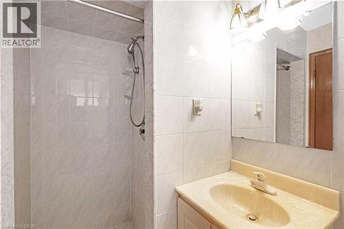 Tiled shower enclosure with an adjustable showerhead, accompanied by a vanity featuring a built-in sink and a wall-mounted light fixture above a mirror - 2535 Privet Crescent, Mississauga, ON - Indoor Photo Showing Bathroom