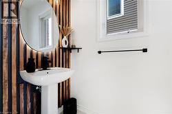 Pedestal sink with a matte black faucet, illuminated oval mirror, wood-slat accent wall, and a single window - 