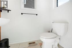 White wall finishes, a wall-mounted towel bar, a window with horizontal blinds, a floating wood-finish shelf, and a white toilet - 