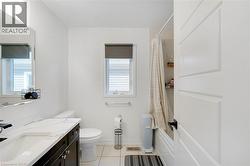 White tile flooring, a dark wood-finish vanity with a light-colored countertop, a white toilet, and a bathtub with a shower - 