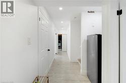 Hallway with recessed lighting, light wood-finish flooring, white paneled doors, and a built-in stainless steel refrigerator - 