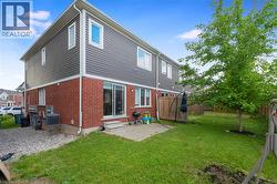 Exterior featuring brick and horizontal siding, a ground-level patio, and a grassy yard with a mature tree - 