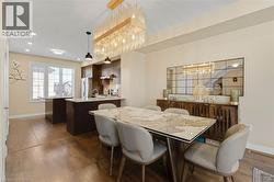 Elegant open-concept dining and kitchen area featuring a marble-top dining table, upholstered dining chairs, dark wood cabinetry, stainless steel appliances, recessed ceiling lighting, and a striking - 
