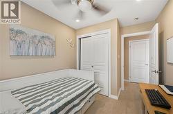 Bright secondary bedroom featuring warm neutral walls, white wainscoting, wood-finish flooring, and a ceiling fan - 