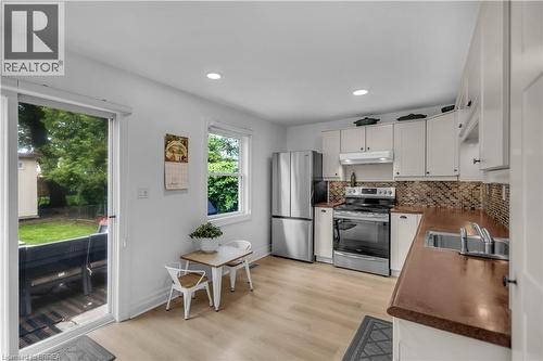 Kitchen featuring light-toned wood-finish flooring, white cabinetry, integrated stainless steel appliances, a mosaic tile backsplash, and a sliding glass door to the exterior - 9 Aylmer Street, Brantford, ON 