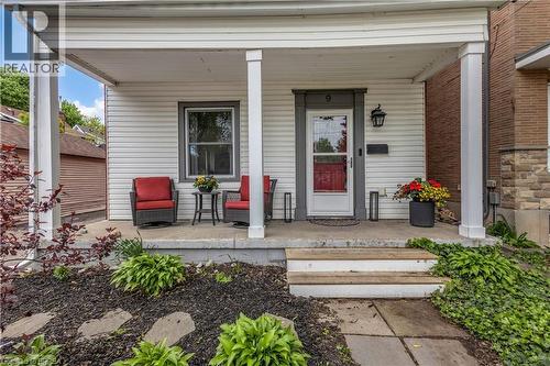 Covered concrete front porch with white columns, white-coloured siding, and a dark-trimmed entry door - 9 Aylmer Street, Brantford, ON 