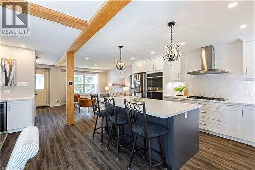 Open-concept kitchen featuring an island with seating, white shaker cabinetry, stainless steel appliances, and wood-finish flooring - 364 Stoneheight Place, Waterloo, ON 