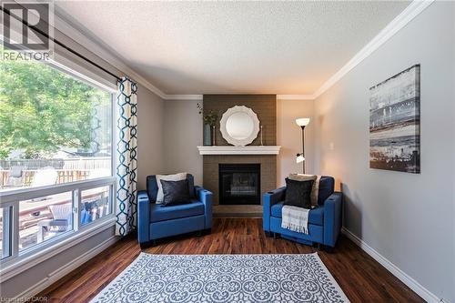 Built-in fireplace with a stone surround and a white mantelpiece, crown molding, wood-finish flooring, and a large window with white trim - 364 Stoneheight Place, Waterloo, ON 