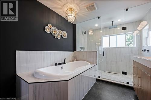 Freestanding soaking tub with a black wall-mounted faucet, glass-enclosed shower with a rain shower head, and an integrated vanity with a single basin - 364 Stoneheight Place, Waterloo, ON 