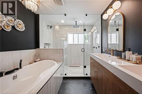 Freestanding soaking tub, glass-enclosed shower, wood-finish double vanity, white countertop with integrated sinks, and gold-tone fixtures - 364 Stoneheight Place, Waterloo, ON 