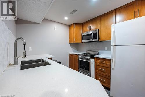 White countertops, wood cabinetry, stainless steel microwave, stainless steel range, and a double basin sink with a gooseneck faucet - 364 Stoneheight Place, Waterloo, ON 