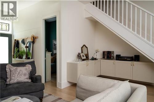 Built-in under-stair storage cabinetry with gold-tone hardware, light wood-finish flooring, and white painted staircase with vertical balusters - 29 Steven Street, Hamilton, ON 