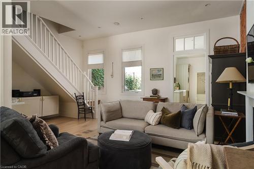 Light wood-finish flooring, white painted staircase with wooden balusters, built-in cabinetry under stairs, transom window above doorway, and wall sconce - 29 Steven Street, Hamilton, ON 