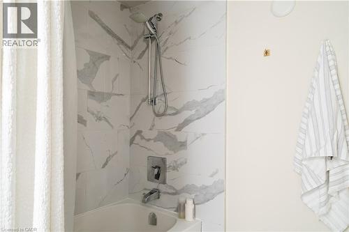 Bathtub with a tiled surround featuring grey veining and a wall-mounted shower fixture - 29 Steven Street, Hamilton, ON 