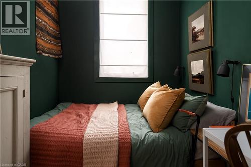 Window with a roller shade, dark green wall finish, and wall-mounted light fixtures - 29 Steven Street, Hamilton, ON 