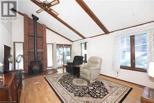 Vaulted ceiling with exposed wood beams, brick fireplace with a wood-burning stove, wood-finish flooring, and multiple windows - 185 Southwood Drive, Kitchener, ON 