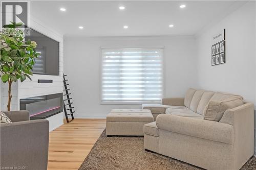 Recessed lighting, wood-finish flooring, white shiplap fireplace surround, built-in linear fireplace, and window with layered shades - 4236 Longmoor Drive, Burlington, ON 