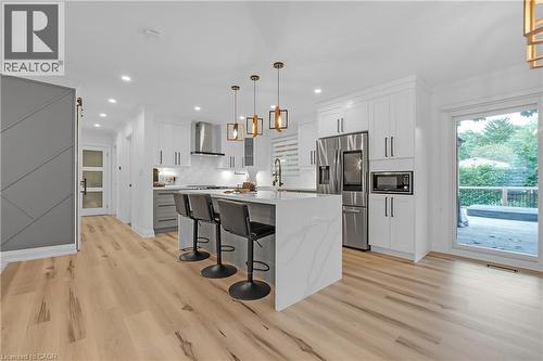 Kitchen featuring a waterfall island with integrated seating, stainless steel appliances, light-finish wood flooring, white cabinetry, and a glass sliding door - 4236 Longmoor Drive, Burlington, ON 