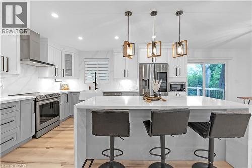 Kitchen featuring wood-finish flooring, white and gray cabinetry, built-in stainless steel appliances, a large center island, and contemporary pendant lighting - 4236 Longmoor Drive, Burlington, ON 