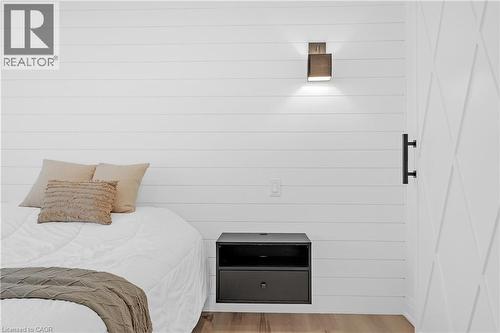 White shiplap wall, wall-mounted sconce lighting, wood-finish flooring, and a white paneled door with black hardware - 4236 Longmoor Drive, Burlington, ON 
