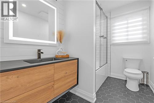 Floating wood-finish vanity with an integrated sink, illuminated mirror, hexagon floor tiles, and a tub with a glass shower enclosure - 4236 Longmoor Drive, Burlington, ON 