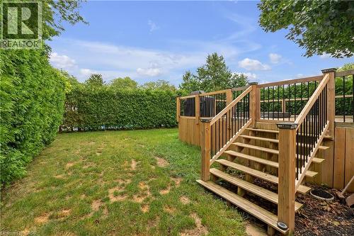 Expansive backyard featuring a natural wood deck with black metal balusters, integrated deck lighting, and a substantial privacy hedge - 4236 Longmoor Drive, Burlington, ON 