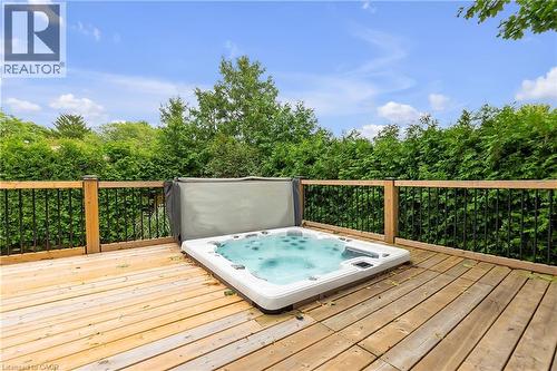 Wood deck with an integrated spa, featuring wood railing posts and black metal balusters, surrounded by mature privacy hedges - 4236 Longmoor Drive, Burlington, ON 