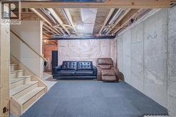 Unfinished basement with exposed ceiling joists and concrete walls, featuring a wood staircase and insulation - 