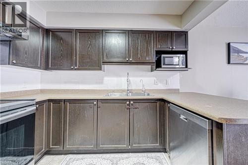 U-shaped kitchen featuring dark wood-finish cabinetry, solid surface countertops, a stainless steel dishwasher, and a built-in microwave - 300 Fallowfield Drive Unit# 21, Kitchener, ON 