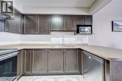 U-shaped kitchen featuring dark wood-finish cabinetry, solid surface countertops, a stainless steel dishwasher, and a built-in microwave - 
