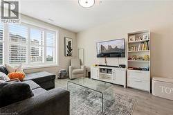 Laminate wood-finish flooring, white plantation shutters, white media console, built-in shelving, and recessed ceiling light - 