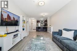Open-concept living area featuring wood-finish flooring throughout, recessed ceiling lighting, and a wall-mounted flat-screen television above white cabinetry with integrated storage - 