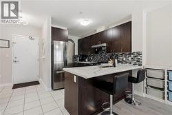 Kitchen featuring dark wood-finish cabinetry, stainless steel appliances, a mosaic tile backsplash, and a white countertop island with an integrated sink - 