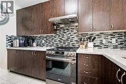 Dark wood-finish cabinetry, mosaic tile backsplash, stainless steel range, and white countertops - 