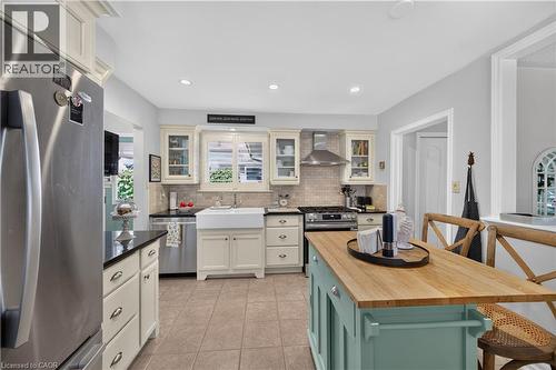Cream cabinetry with dark countertops, stainless steel appliances, a white farmhouse sink, and a center island with a wood-finish top - 1434 Dewbourne Crescent, Burlington, ON 