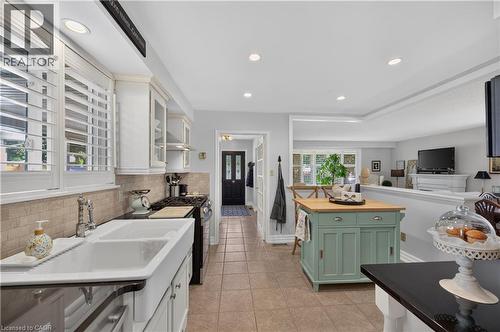 White cabinetry with glass-front accents, farmhouse-style double basin sink, black countertop, recessed lighting, and tile flooring - 1434 Dewbourne Crescent, Burlington, ON 