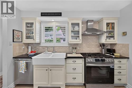 Stainless steel appliances, light-toned cabinetry, subway tile backsplash, farmhouse-style sink, and solid surface countertops - 1434 Dewbourne Crescent, Burlington, ON 