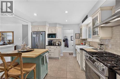 Kitchen featuring tiled flooring, white cabinetry, stainless steel appliances, a center island with a wood countertop, and a farmhouse sink - 1434 Dewbourne Crescent, Burlington, ON 