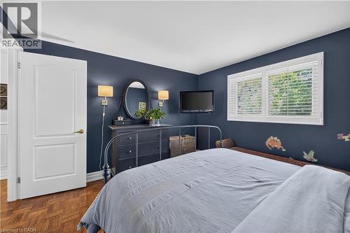 Wood-finish flooring with a herringbone pattern, white interior door with panel detailing, white window with horizontal blinds, and a wall-mounted television - 1434 Dewbourne Crescent, Burlington, ON 