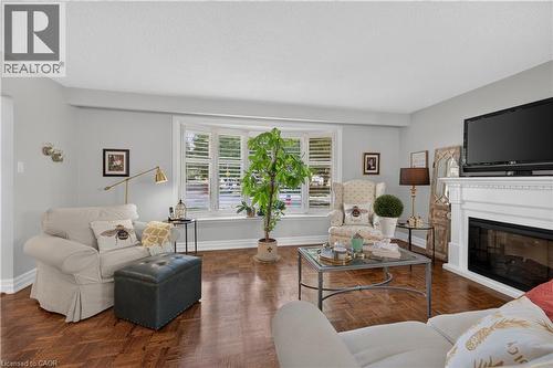 Bay window with white plantation shutters, rich wood-finish flooring, and a white fireplace with a mantel - 1434 Dewbourne Crescent, Burlington, ON 