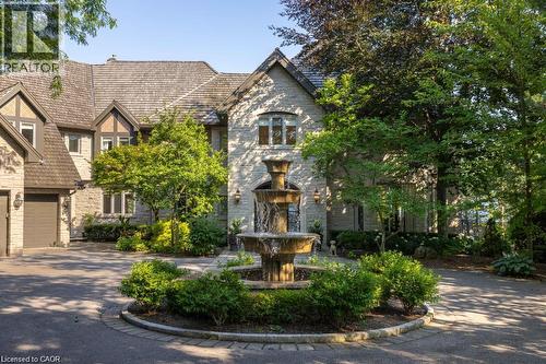 Stone exterior residence with a multi-tiered fountain centerpiece, mature landscaping, and an attached two-car garage - 4038 Lakeshore Road, Burlington, ON 