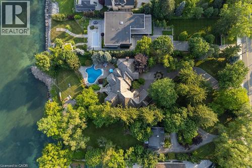 Waterfront property featuring extensive mature landscaping, a freeform swimming pool, and a stone-clad multi-level residence with a gabled roof - 4038 Lakeshore Road, Burlington, ON 