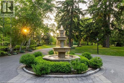 Circular paver driveway featuring a multi-tiered water fountain, surrounded by manicured shrubs - 4038 Lakeshore Road, Burlington, ON 