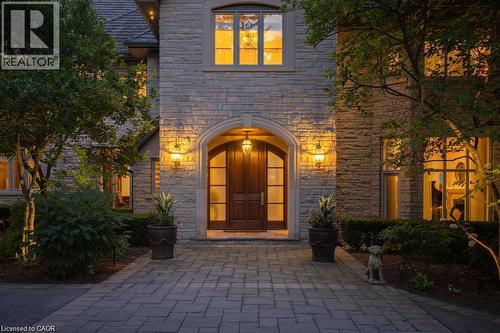 Stone exterior facade with a prominent arched entry, wood-paneled double doors, and decorative outdoor lighting - 4038 Lakeshore Road, Burlington, ON 