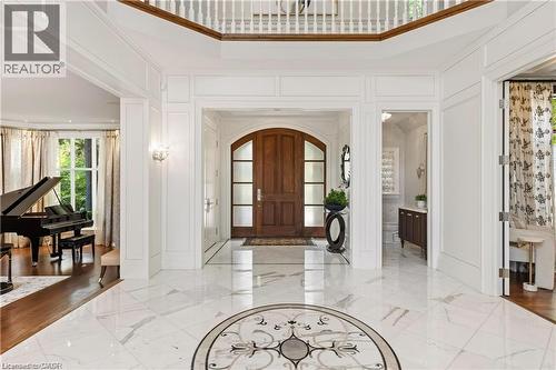 Grand entryway featuring marble flooring with an inlaid medallion, a solid wood arched entry door, extensive wall paneling, and a staircase with a wood handrail - 4038 Lakeshore Road, Burlington, ON 