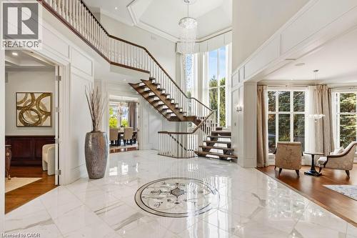 Soaring ceiling with a tiered chandelier, grand staircase with wood treads and white balusters, polished tile flooring with an inlaid medallion, and expansive windows - 4038 Lakeshore Road, Burlington, ON 